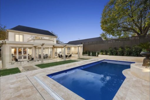 Travertine paving in beige and cream with a dark blue pool in large backyard